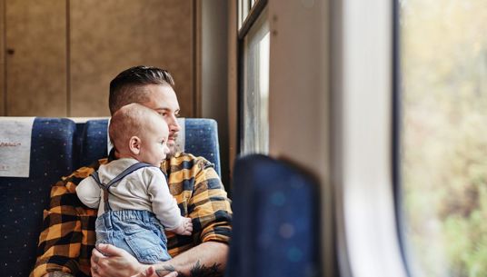 Bild på pappa och son som sitter och tittar ut genom fönstret ombord på ett Krösatåg.